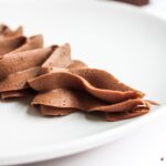 Close-up of smooth chocolate buttercream piped in swirls on a white plate, showcasing creamy texture and consistency.