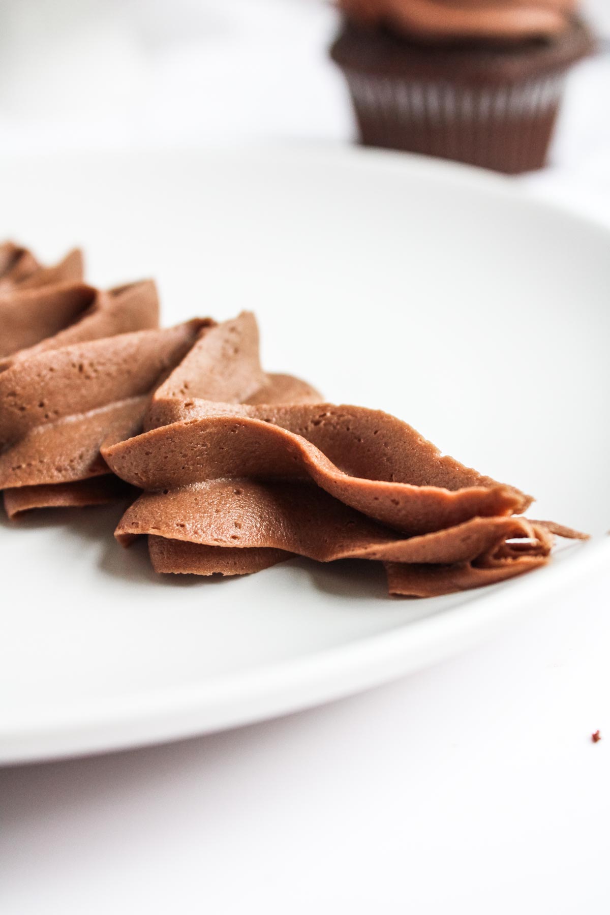 Close-up of smooth chocolate buttercream piped in swirls on a white plate, showcasing creamy texture and consistency.